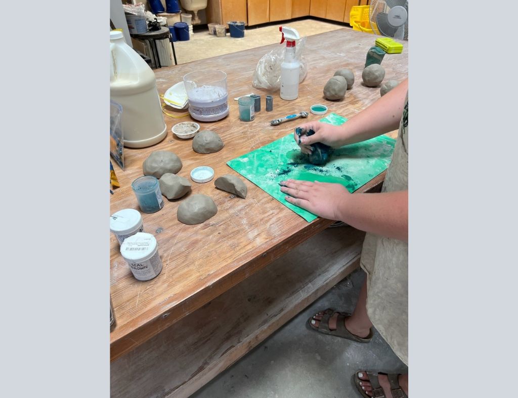 Shannon begins the process of marbling the clay by adding powder pigment and folding it in, using a wedging technique.